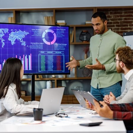 Motivated african american businessman having business meeting with managers, negotiating, using presentation tv with statistics, charts, big data. Digital entrepreneurs work on an e-commerce project