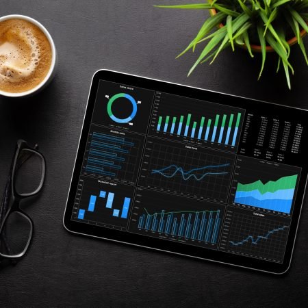 Tablet with business reports and charts, coffee cup and office supplies on desk. Top view flat lay