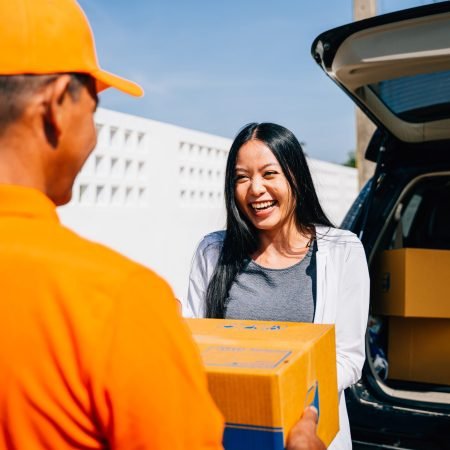 Modern home delivery depicted as a courier in uniform delivers a cardboard parcel to a smiling woman at her house emphasizing efficient delivery service and customer happiness.